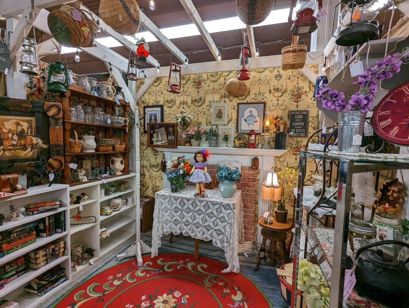 A vendor booth at Nostalgia: shelves of china and teapots, framed pictures on the wall and a red patterned rug.
