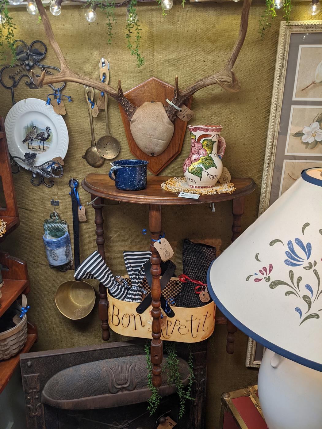 A styled wall at Nostalgia hung with ceramic plates, a mounted antler, lamps and a lettered sign.